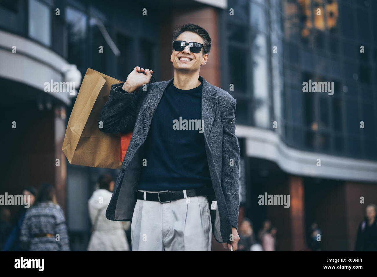 Grave ragazzo fantastico con occhiali da sole e di sacchetti di carta a piedi la strada. Foto Stock