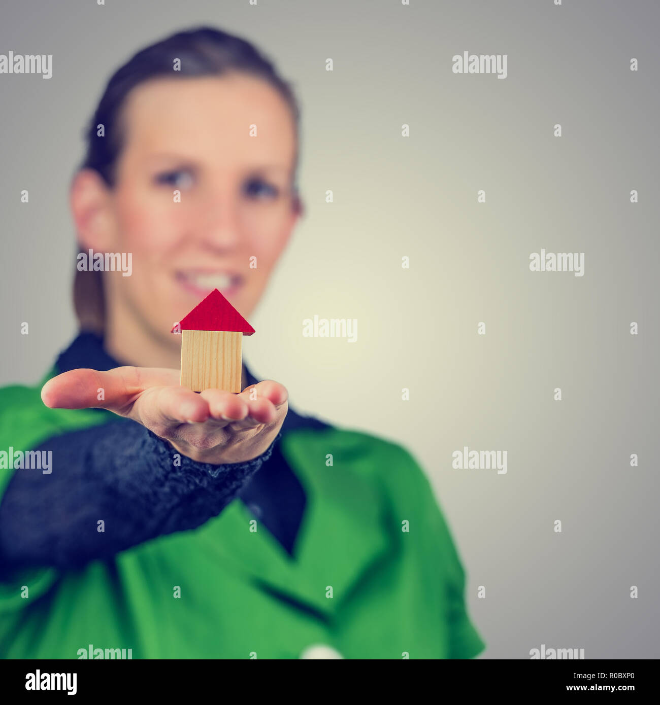 Retro vintage o instagram stile immagine di un sorridente giovane agente immobiliare tenendo fuori un modello di casa sul palmo della sua mano concettuale del real estat Foto Stock