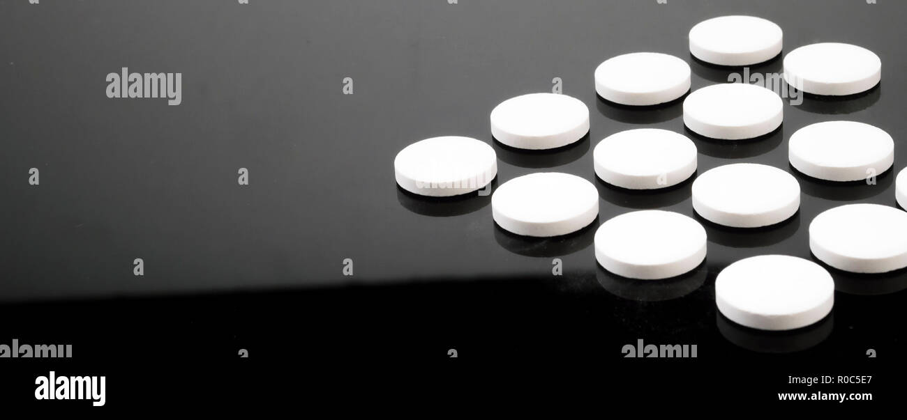 Alcune pillole bianchi allineati isolati su sfondo nero, immagine concettuale Foto Stock