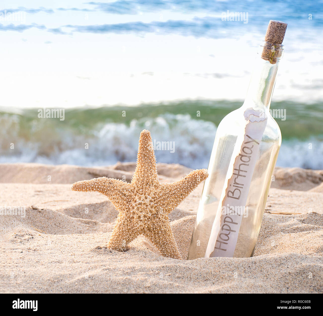 Close up di stelle marine e buon compleanno un messaggio in bottiglia in riva al mare con fondo di acqua Foto Stock