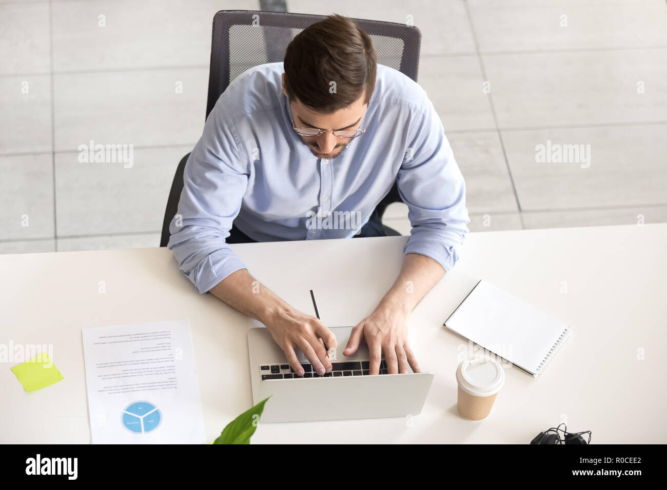 Imprenditore lavora su laptop seduto alla scrivania in ufficio, vista dall'alto Foto Stock