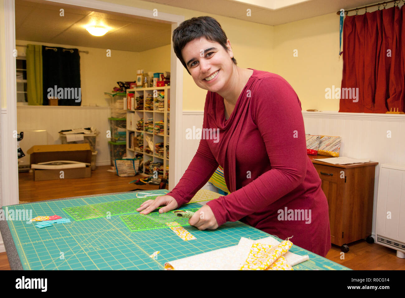 Sorridente persona che lavora con una griglia in tessuto e la taglierina nella loro camera artigianale Foto Stock