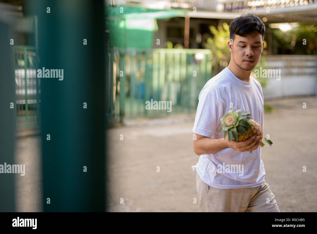 Giovane uomo asiatico portando ananas a casa Foto Stock