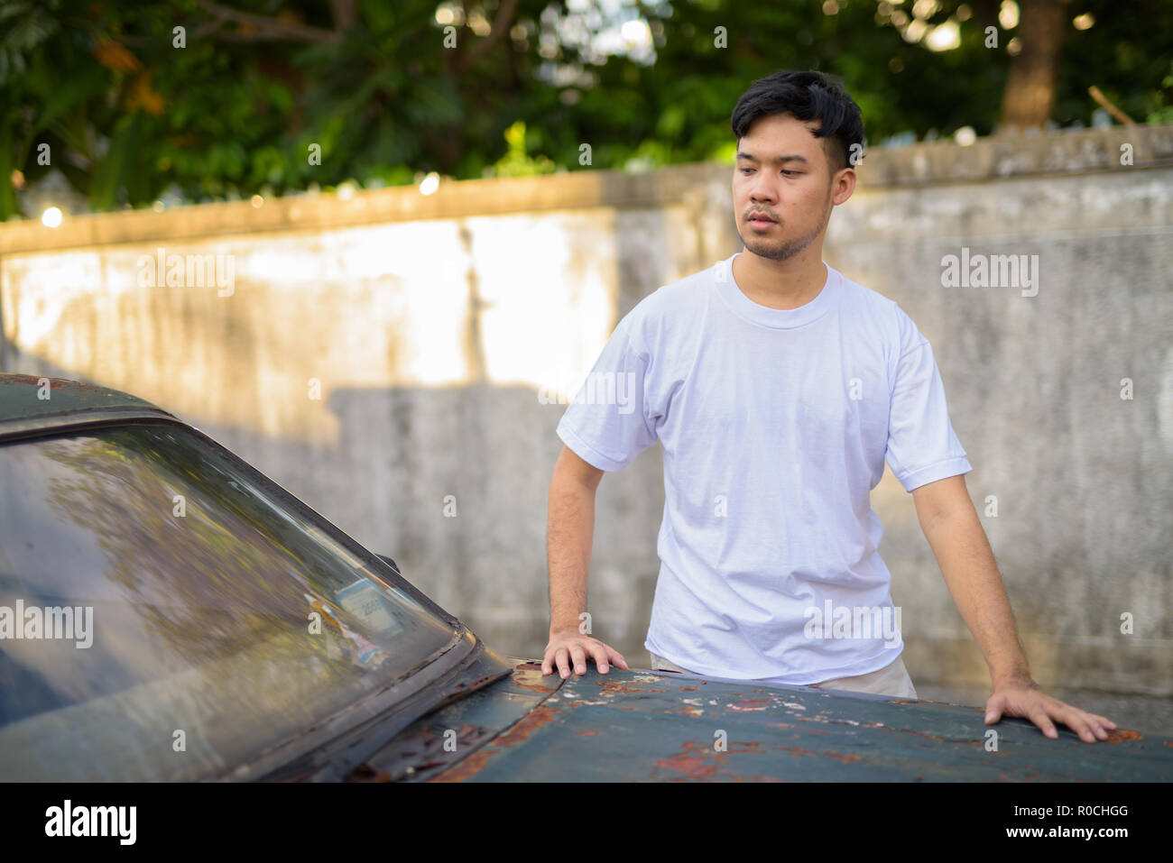 Giovane uomo asiatico con vecchio arrugginito in auto le strade all'aperto Foto Stock