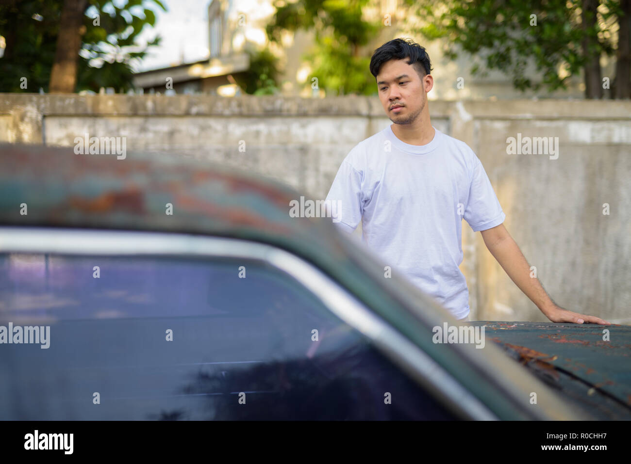 Giovane uomo asiatico con vecchio arrugginito in auto le strade all'aperto Foto Stock