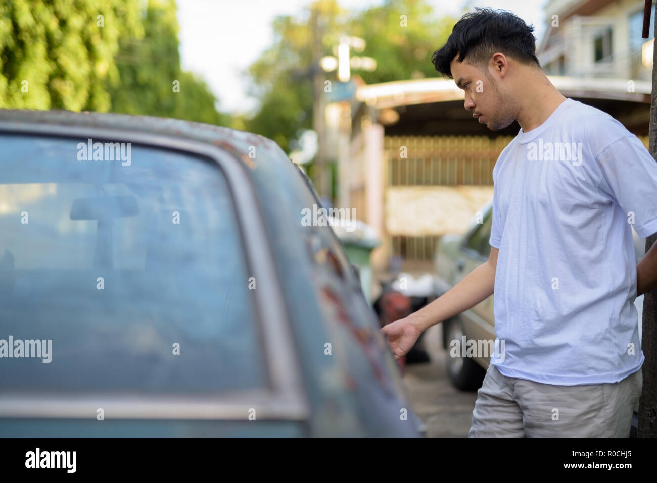 Giovane uomo asiatico con vecchio arrugginito in auto le strade all'aperto Foto Stock