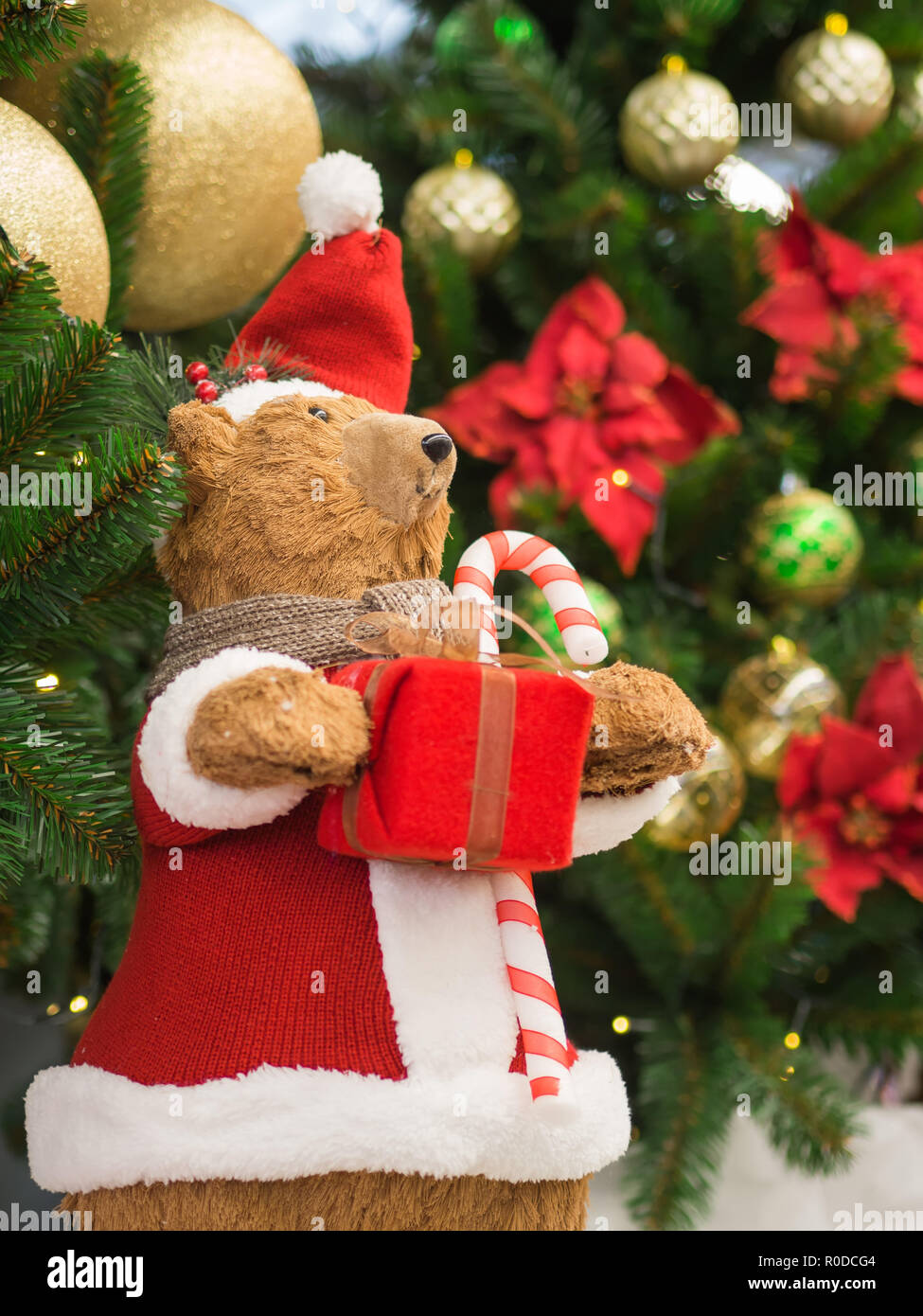 Un giocattolo portano vestiti da Babbo Natale in piedi contro un albero di Natale in possesso di una confezione regalo. Natale e Anno Nuovo concetto. Foto Stock