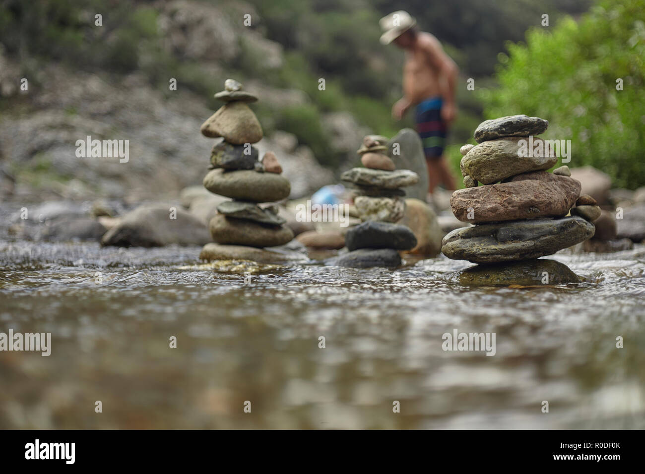 Pile di rocce zen in un dissipatore di montagna con un uomo sfigurato in background che attraversa il flusso stesso. Foto Stock