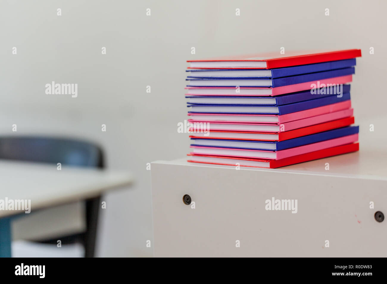 Pila di notebook multicolore su un cassetto con arredi scolastici in background Foto Stock