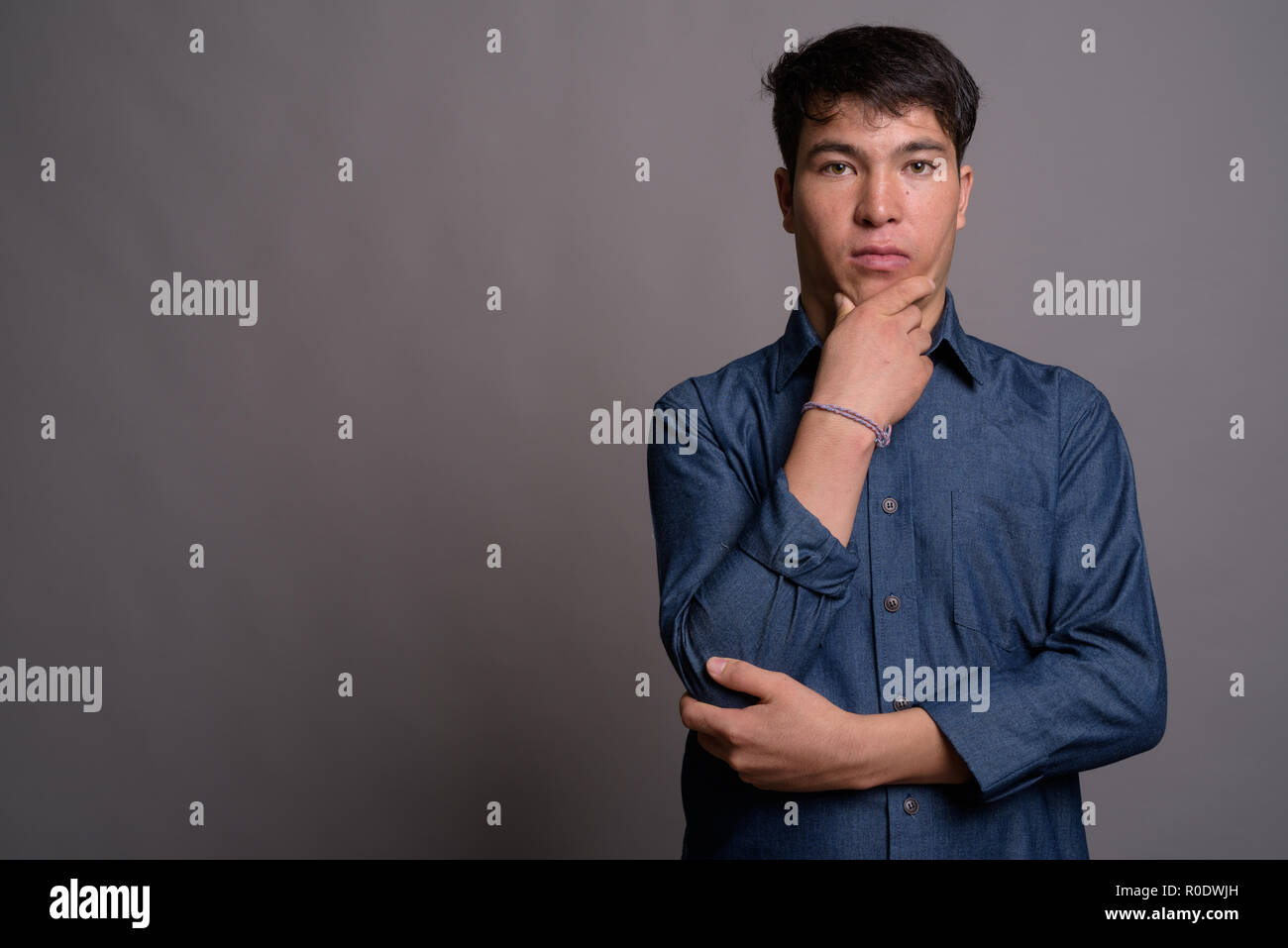 Giovane uomo asiatico indossando maglietta blu contro uno sfondo grigio Foto Stock