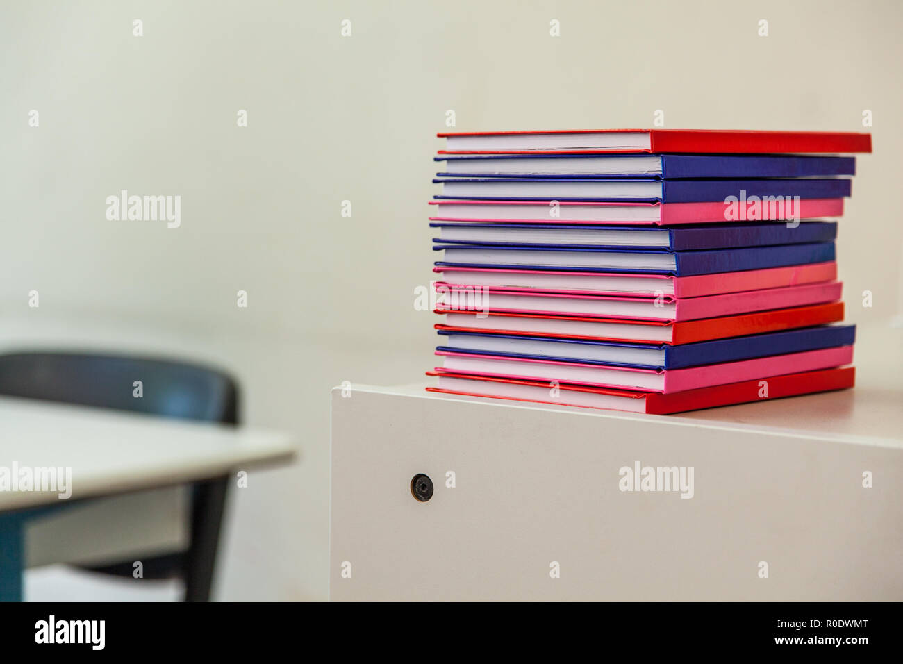 Pila di notebook multicolore su un cassetto con arredi scolastici in background Foto Stock