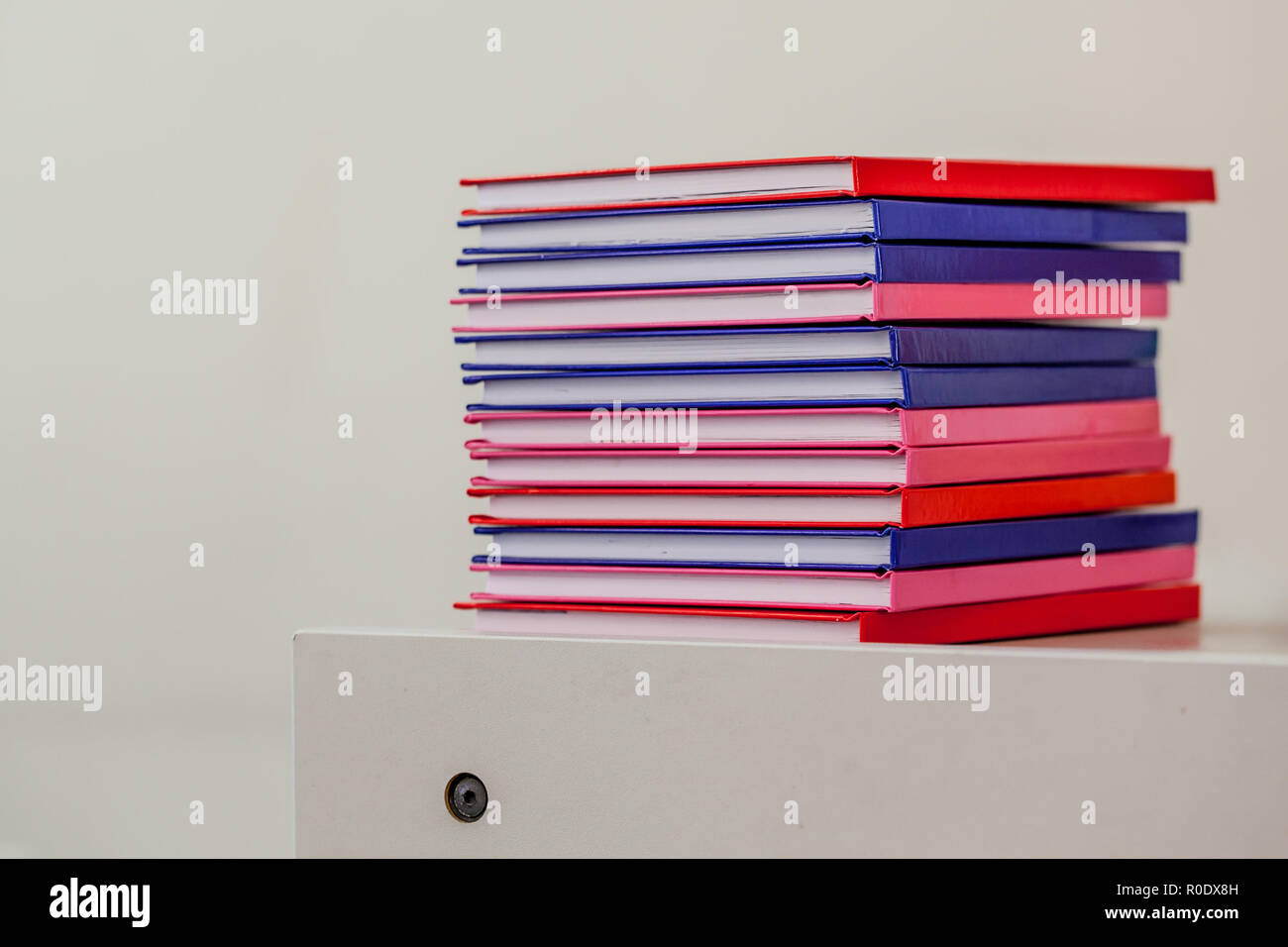 Pila di notebook multicolore su un cassetto con arredi scolastici in background Foto Stock