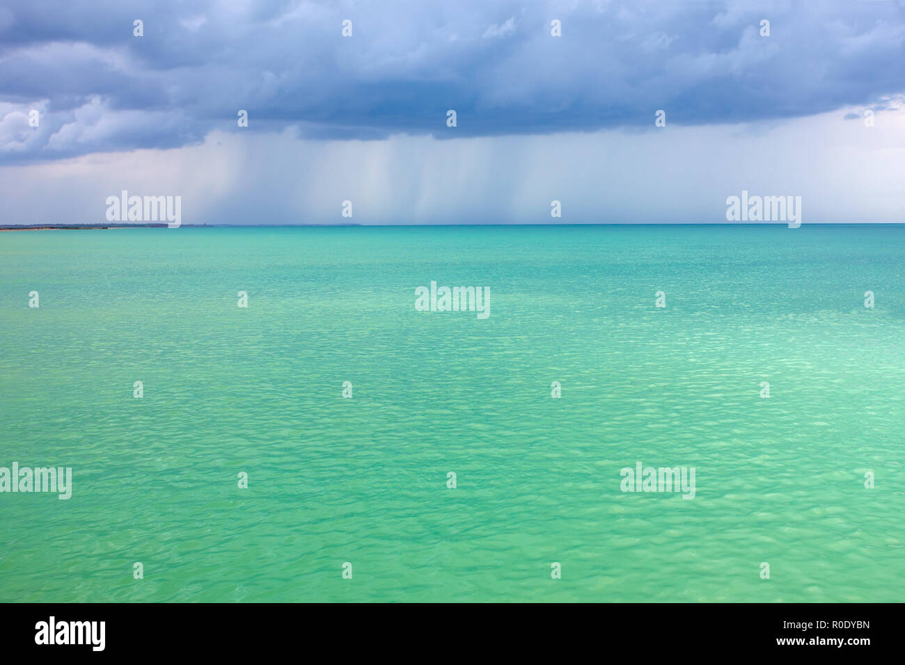 Nuvole di tempesta di pioggia sul mare con un turchese superficie illuminata dal sole Foto Stock