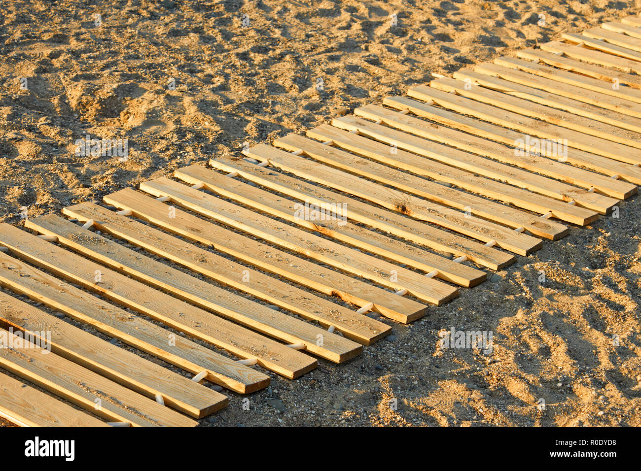 Lungo il tappetino in legno realizzato da nuove tavole parallele giacenti su di una spiaggia di sabbia Foto Stock