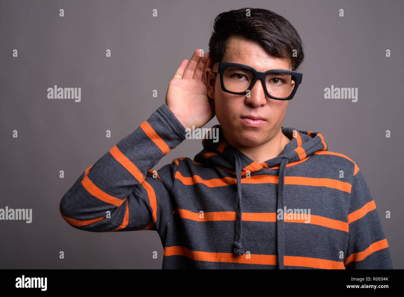 Giovani asiatici nerd uomo che indossa hoodie contro uno sfondo grigio Foto Stock