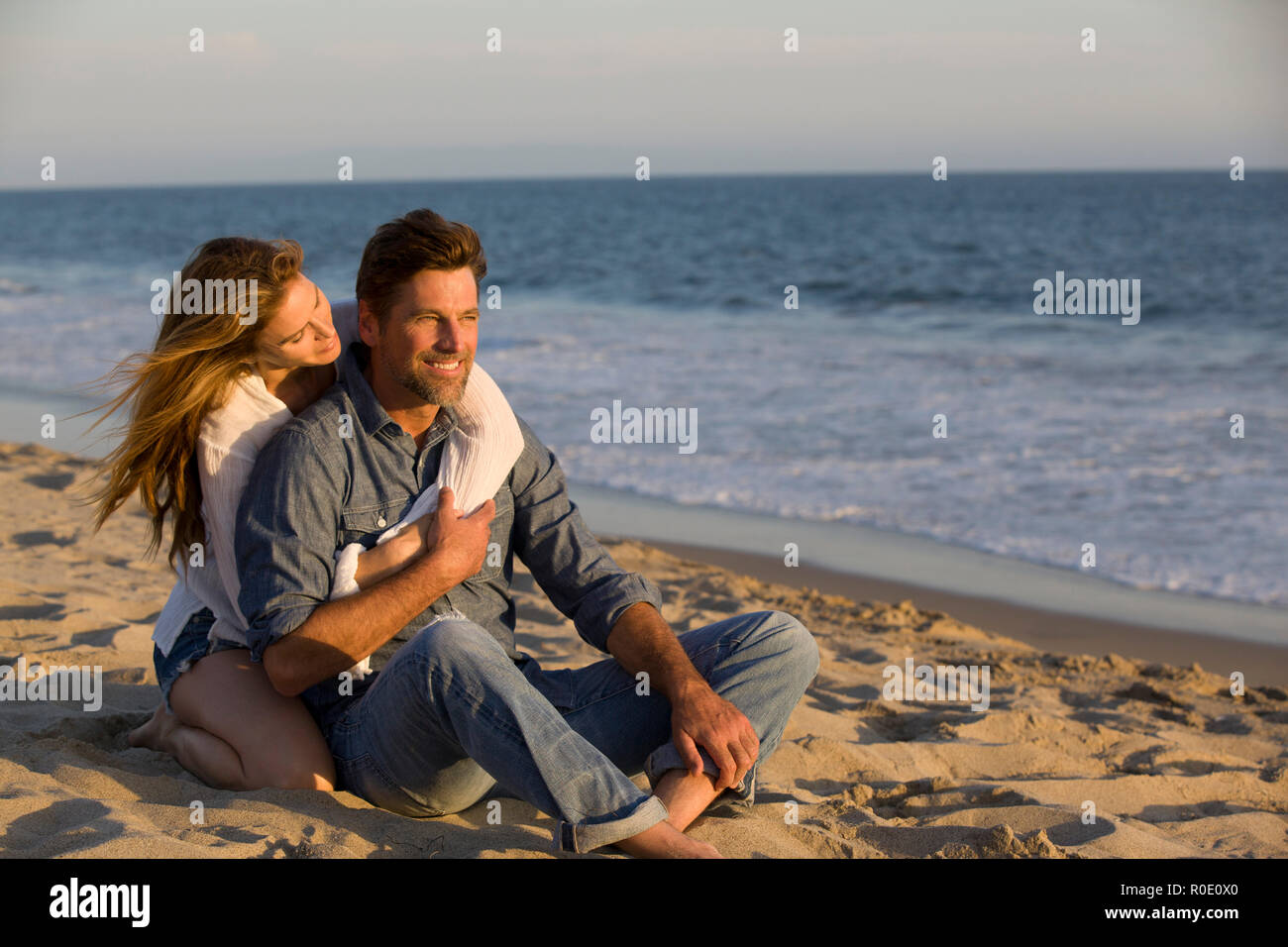 Affettuosa Mid-Adult giovane seduto sulla spiaggia sabbiosa Foto Stock