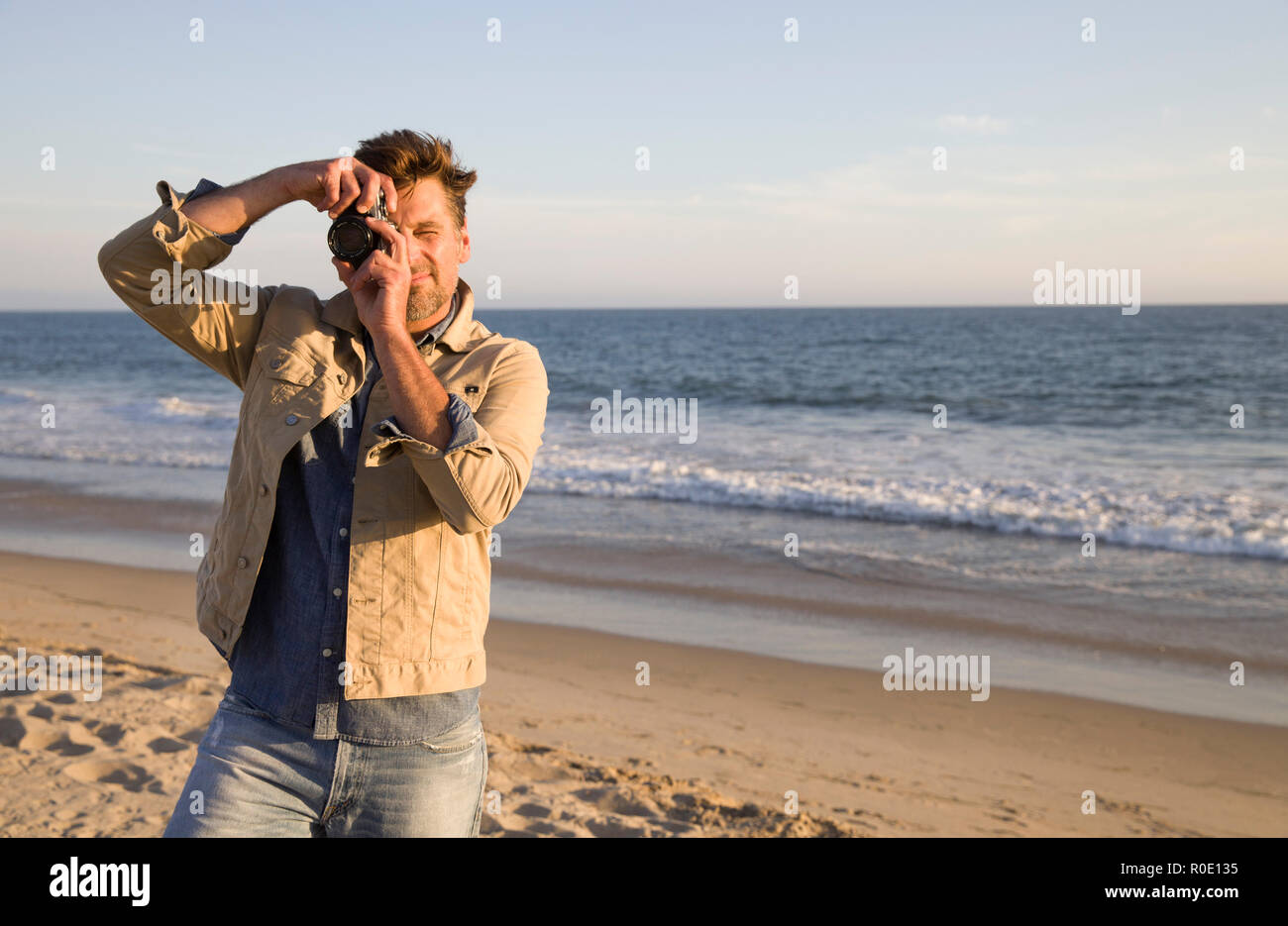 Uomo Mid-Adult guardando attraverso la lente della fotocamera in spiaggia Foto Stock