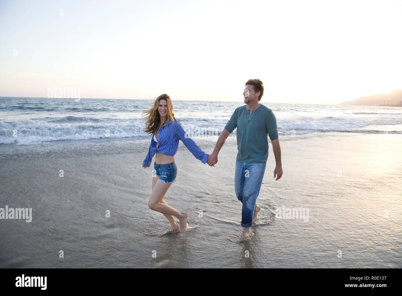 Romantico Mid-Adult giovane tenendo le mani mentre passeggiate lungo la spiaggia Foto Stock
