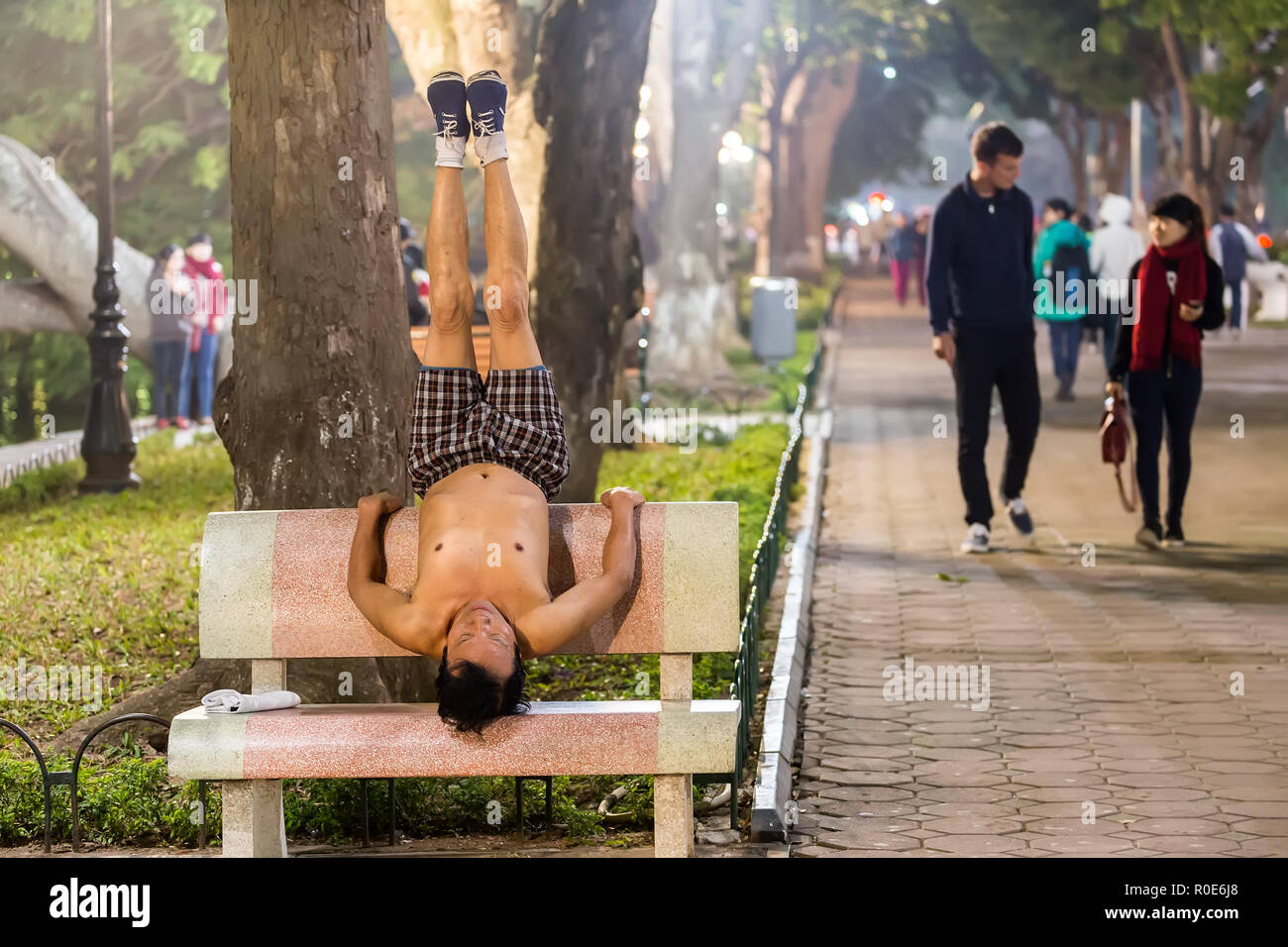 HANOI, Vietnam, dicembre 15, 2014: un uomo è la pratica dello Yoga su un banco di pubblico in serata presso il centro della città è il lago Hoan Kiem nella città di Hanoi, Vietnam. Foto Stock