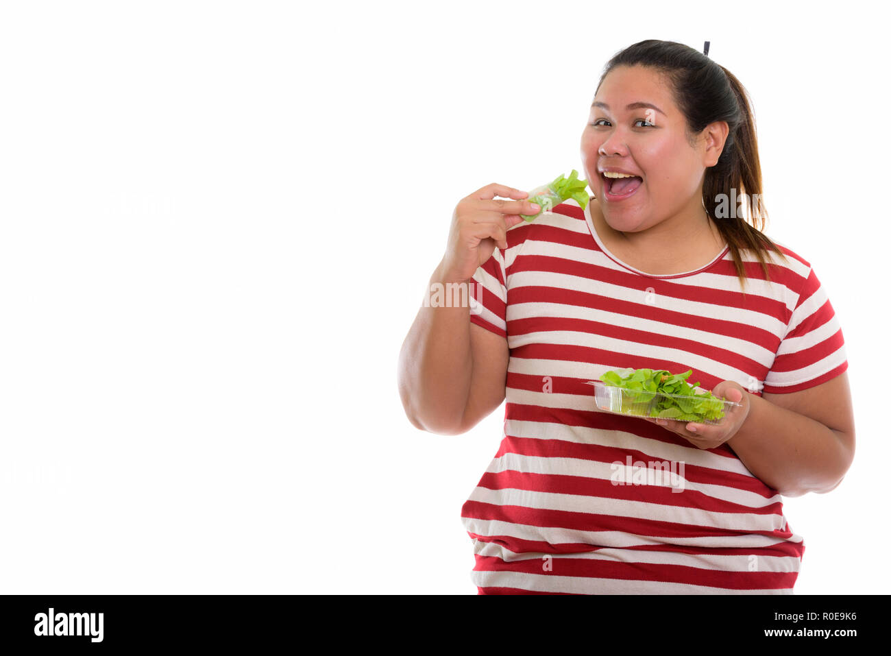 Studio shot di giovani felici fat Asian donna sorridente mentre mangia Foto Stock