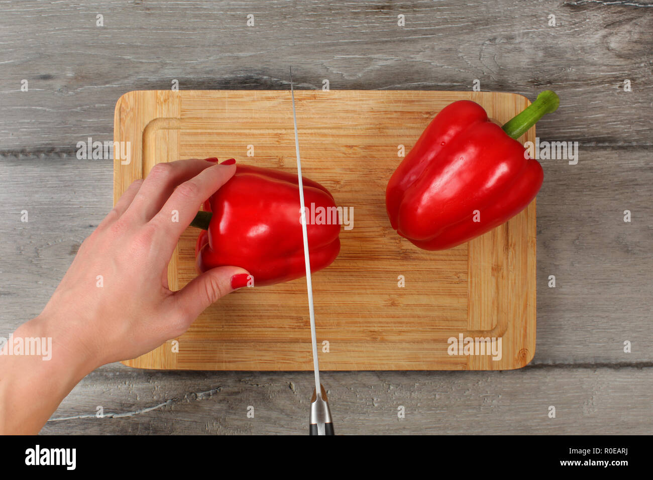 Vista del piano portapaziente - donna il taglio di peperone rosso sul tagliere con un coltello da chef. Dettaglio a portata di mano Foto Stock