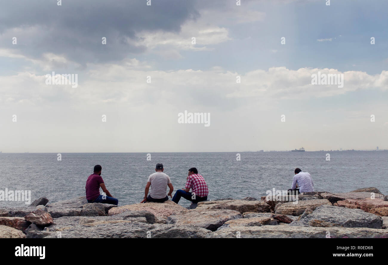Vista di quattro irriconoscibile uomini seduti sulle rocce dal Bosforo. Immagine è catturata nel quartiere chiamato Moda situato sul lato Asiatico di Ista Foto Stock