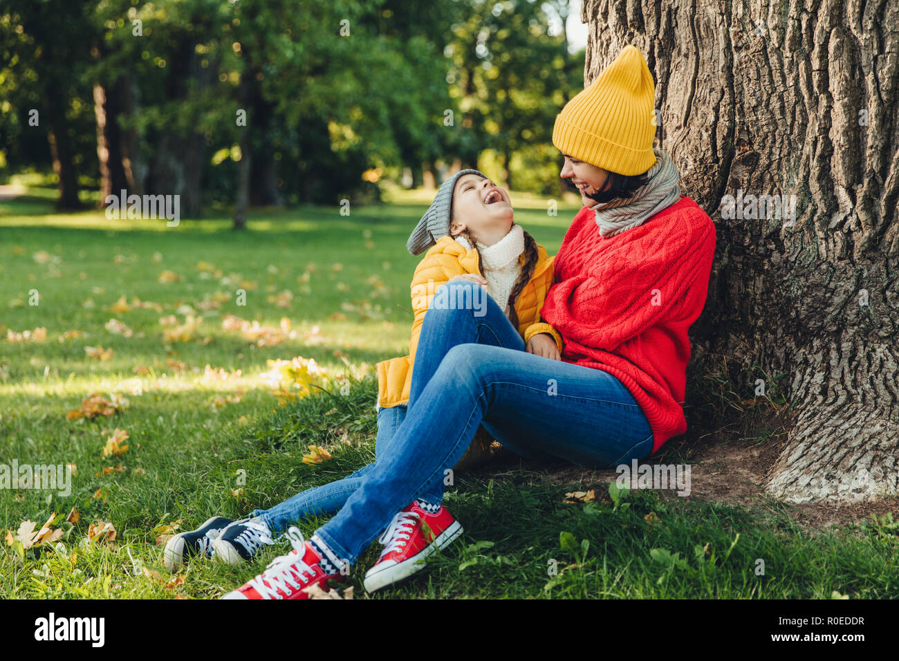 Ritratto di attraente modello femminile, ha una piacevole conversazione con la figlia e il resto su erba verde, cercare fortuna avere gioia. Bella donna con piccole gir Foto Stock