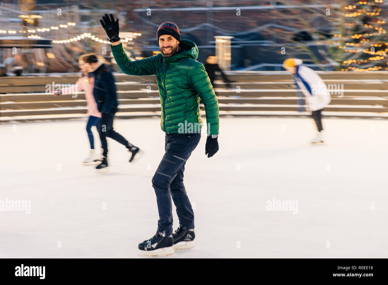 Felice onde maschio con mano come avvisi il suo amico sulla pista di pattinaggio, hanno il desiderio di skate insieme, gioisce incontro, ha un buon tempo e umore, intrattiene Foto Stock