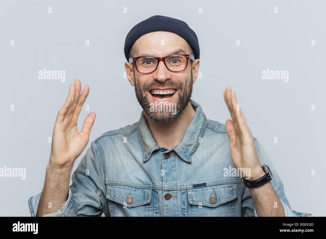 Bel uomo felice alza le mani con garantite, ha detto contentissimo espressione, guarda con piacere il viso, è folta barba e baffi. Felice l'uomo in eyewear Foto Stock