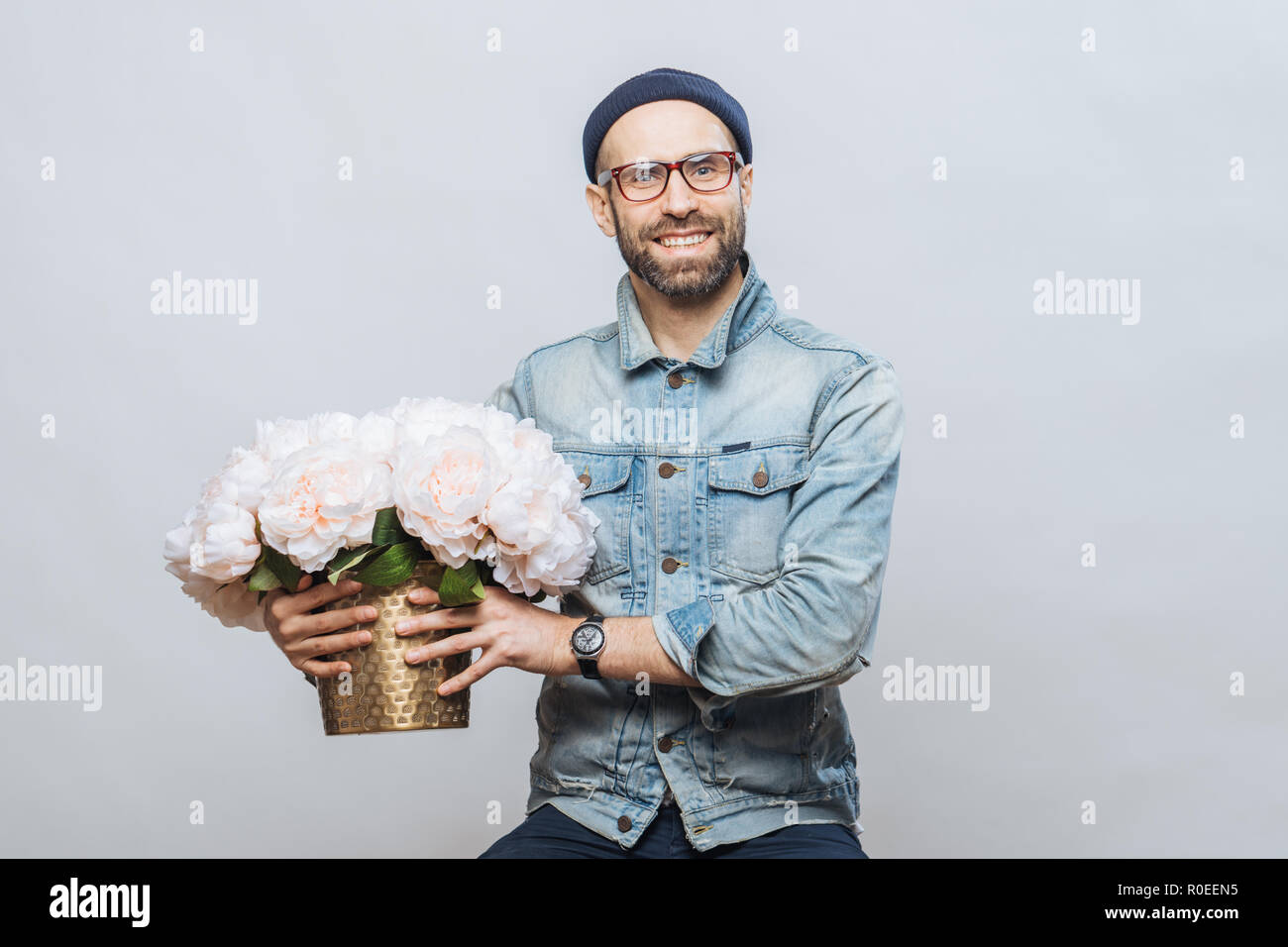 Felice felice maschio acquista un mazzo di fiori per la speciale occasione, indossa camicia di jeans e maglietta denim, isolato su sfondo bianco. Emotiona gioiosa Foto Stock