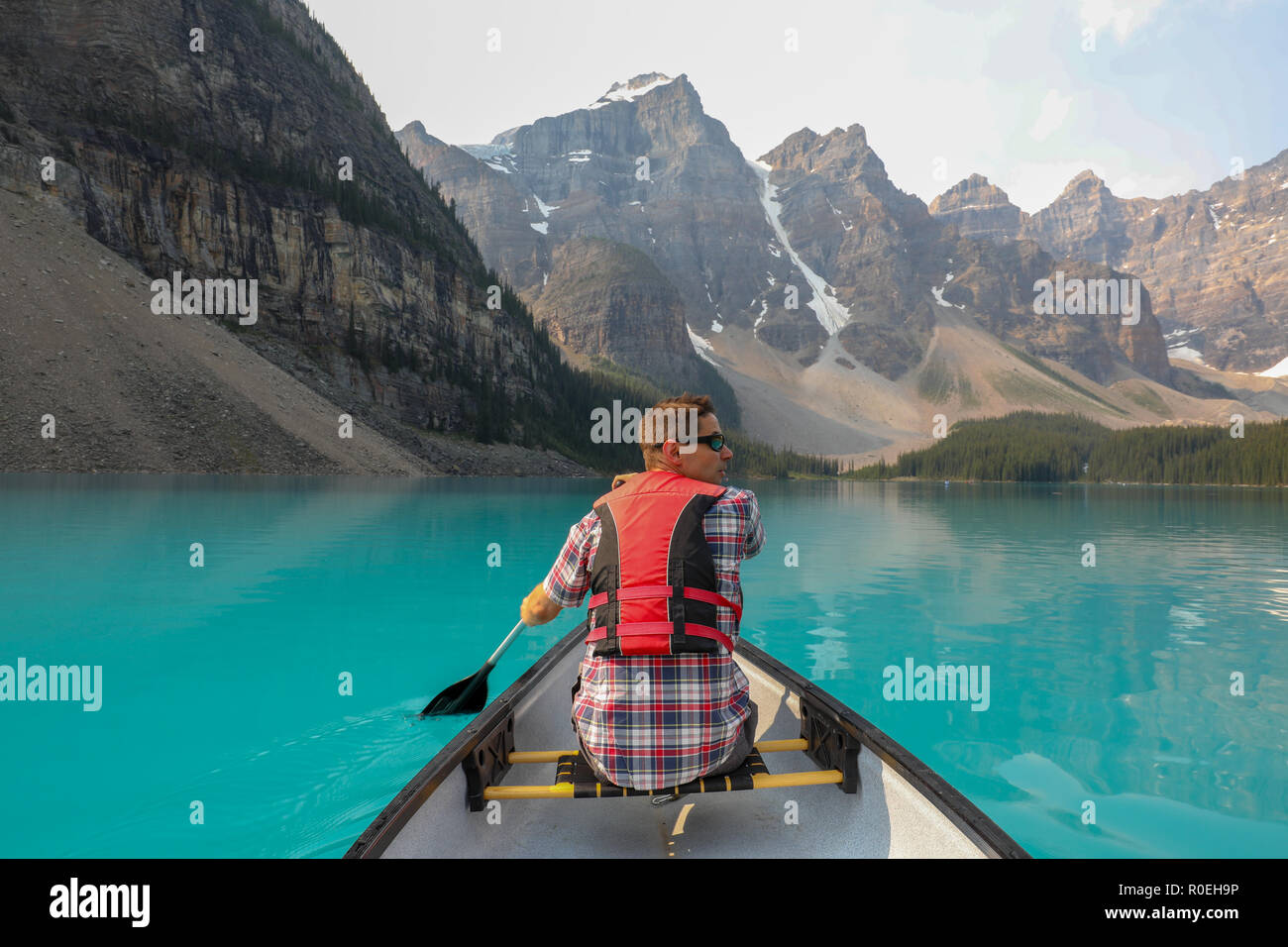 Maschio su una canoa con red giubbotto di salvataggio sul Lago Moraine con Montagne Rocciose nel Parco Nazionale di Banff, Canada Foto Stock