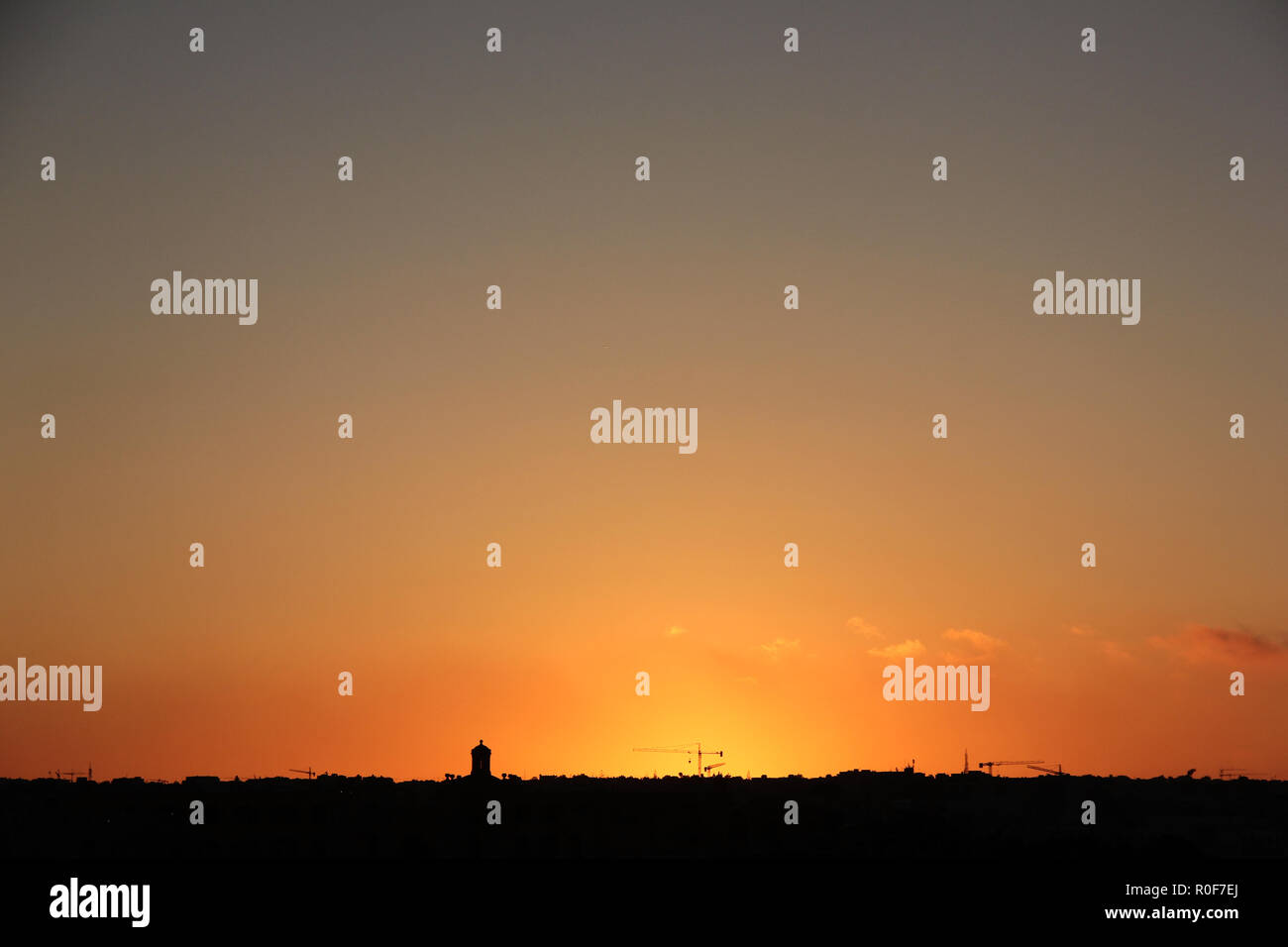 Arancione tramonto Cielo sopra la silhouette della città di torri e gru edili Foto Stock