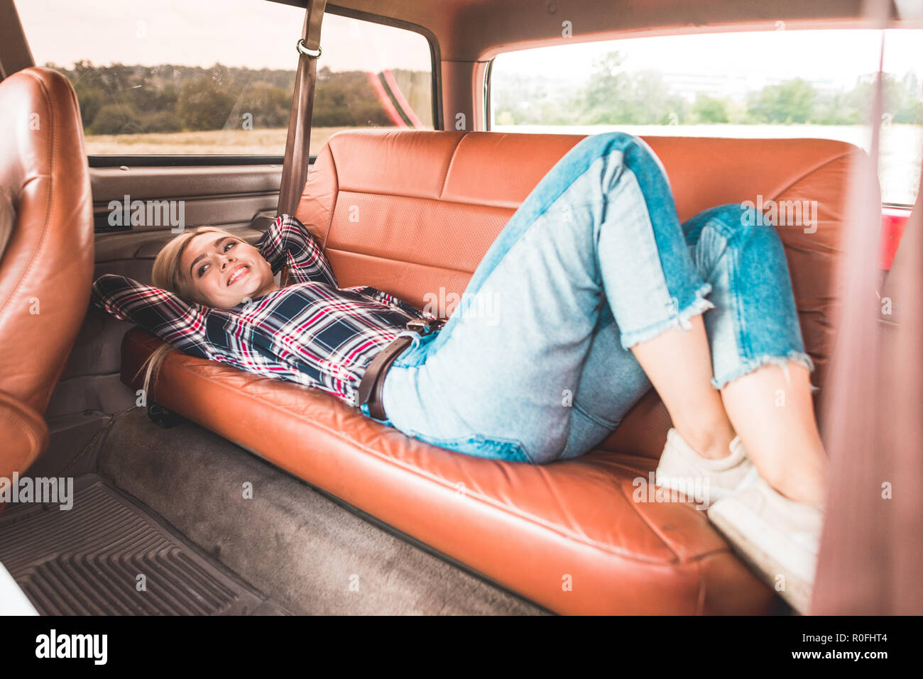 Bella giovane donna sdraiata sul sedile posteriore della vettura vintage nel campo Foto Stock