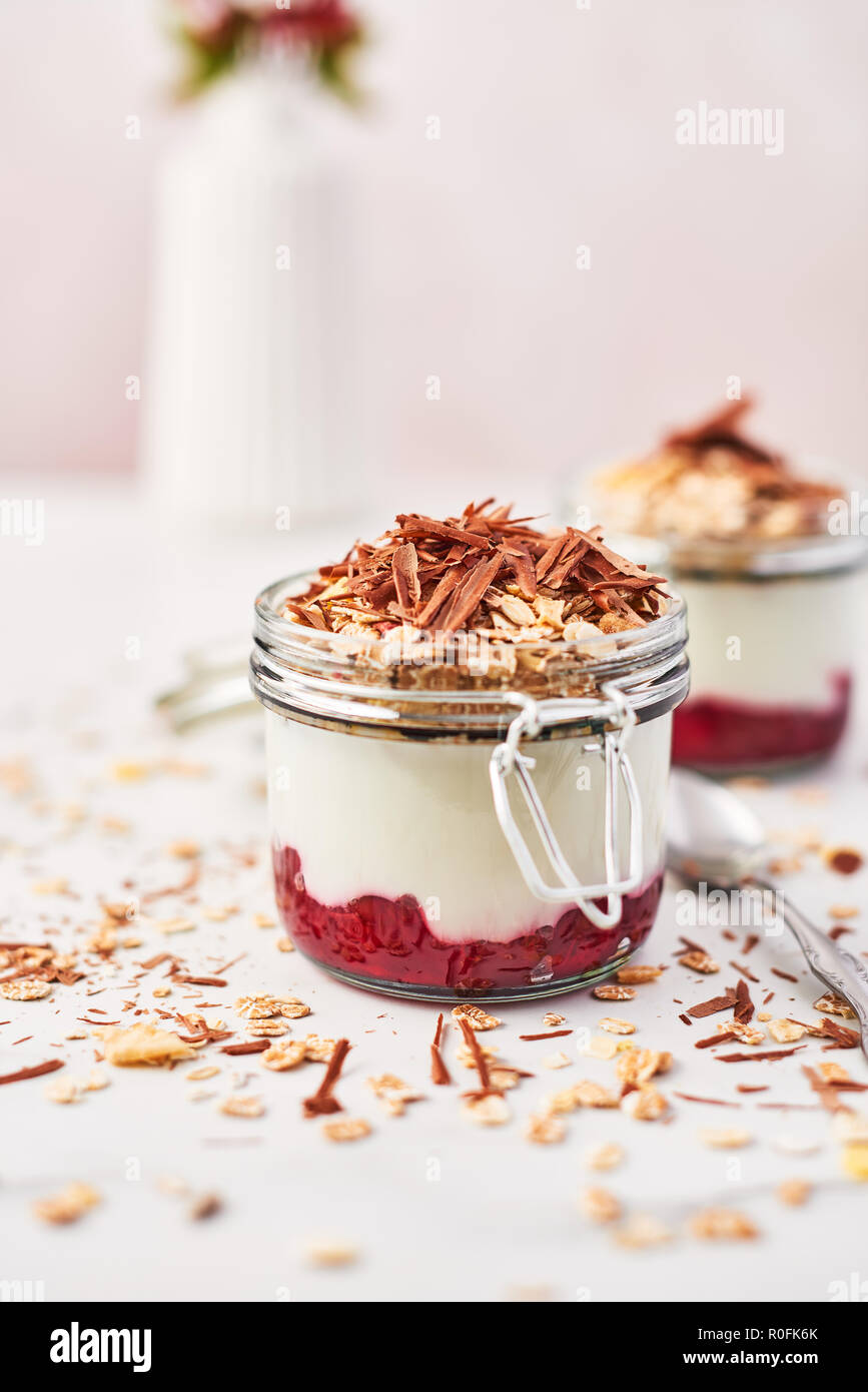 Una sana prima colazione. Due vasetti di yogurt sano con salsa di fragole, avena e cioccolato bianco sulla tavola di marmo. Close up con copia spazio. Foto Stock