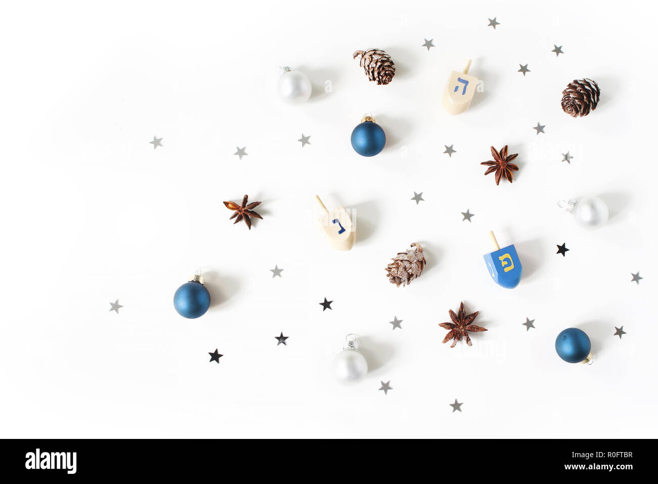 Hanukkah elegante composizione madre. Motivo decorativo. Legno giocattoli dreidel, larice coni, anice e argento coriandoli stelle decorazione su sfondo bianco. Appartamento laico, vista dall'alto. Design ebraica. Foto Stock