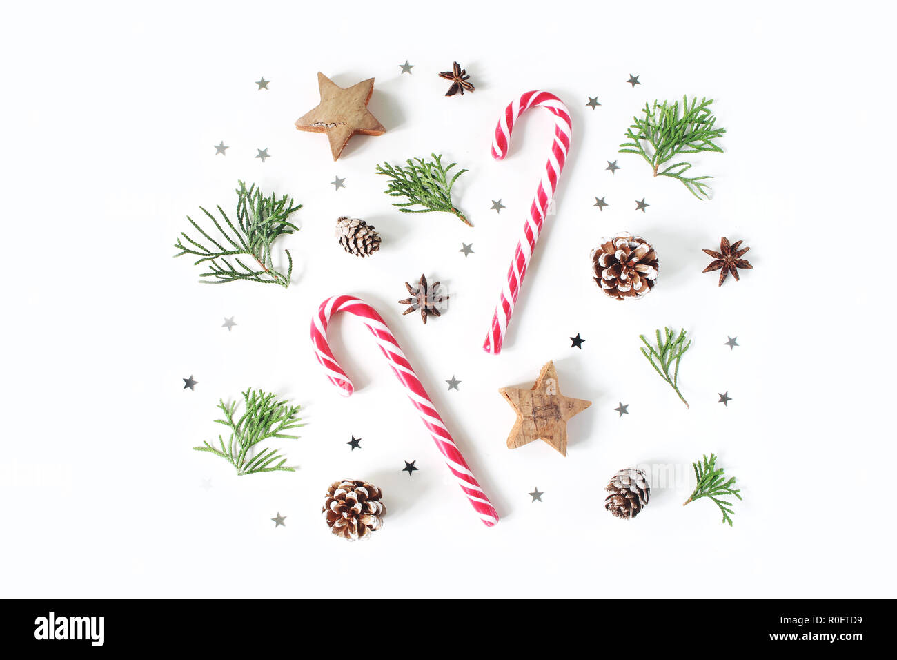 Composizione di natale. Decorative pattern invernale, banner fatte di rami di cipresso, pigne, candy canes, anice, in legno e in argento coriandoli stelle. Tavolo bianco sullo sfondo. Appartamento laico, vista dall'alto. Foto Stock