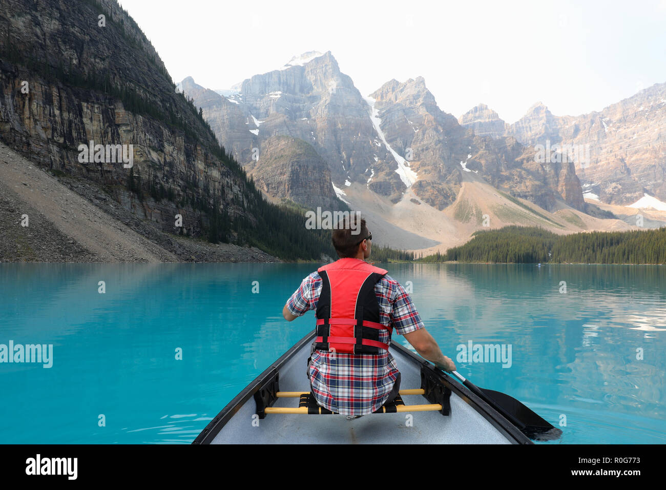 Maschio su una canoa con red giubbotto di salvataggio sul Lago Moraine con Montagne Rocciose nel Parco Nazionale di Banff, Canada Foto Stock