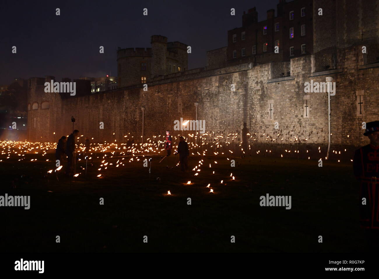 Yeoman Warders ('Beefeaters') che illumina la prima di migliaia di fiamme in una cerimonia di illuminazione nel fossato asciutto della Torre di Londra come parte di un'installazione chiamata Beyond the Deepening Shadow: La Torre ricorda, per celebrare il centenario della fine della prima guerra mondiale. Foto Stock