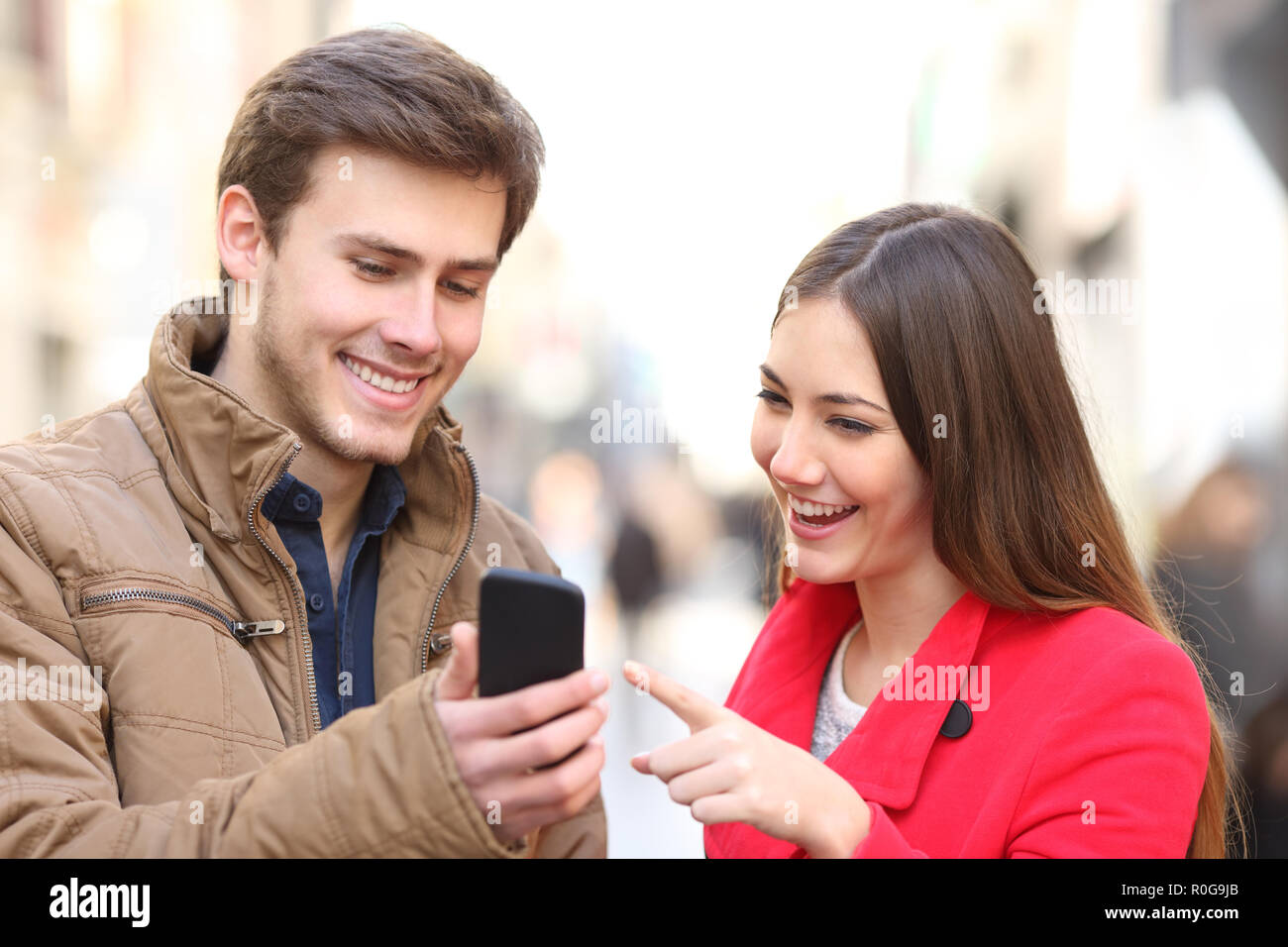 Felice coppia controllo smart phone contenuto in inverno in strada Foto Stock
