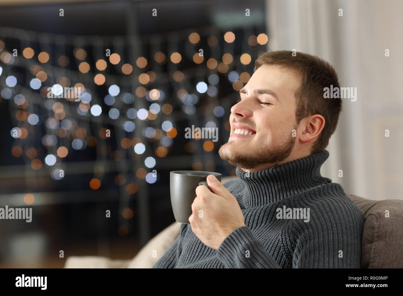 Uomo felice godendo di caffè nella notte seduto su un divano nel salotto di casa Foto Stock