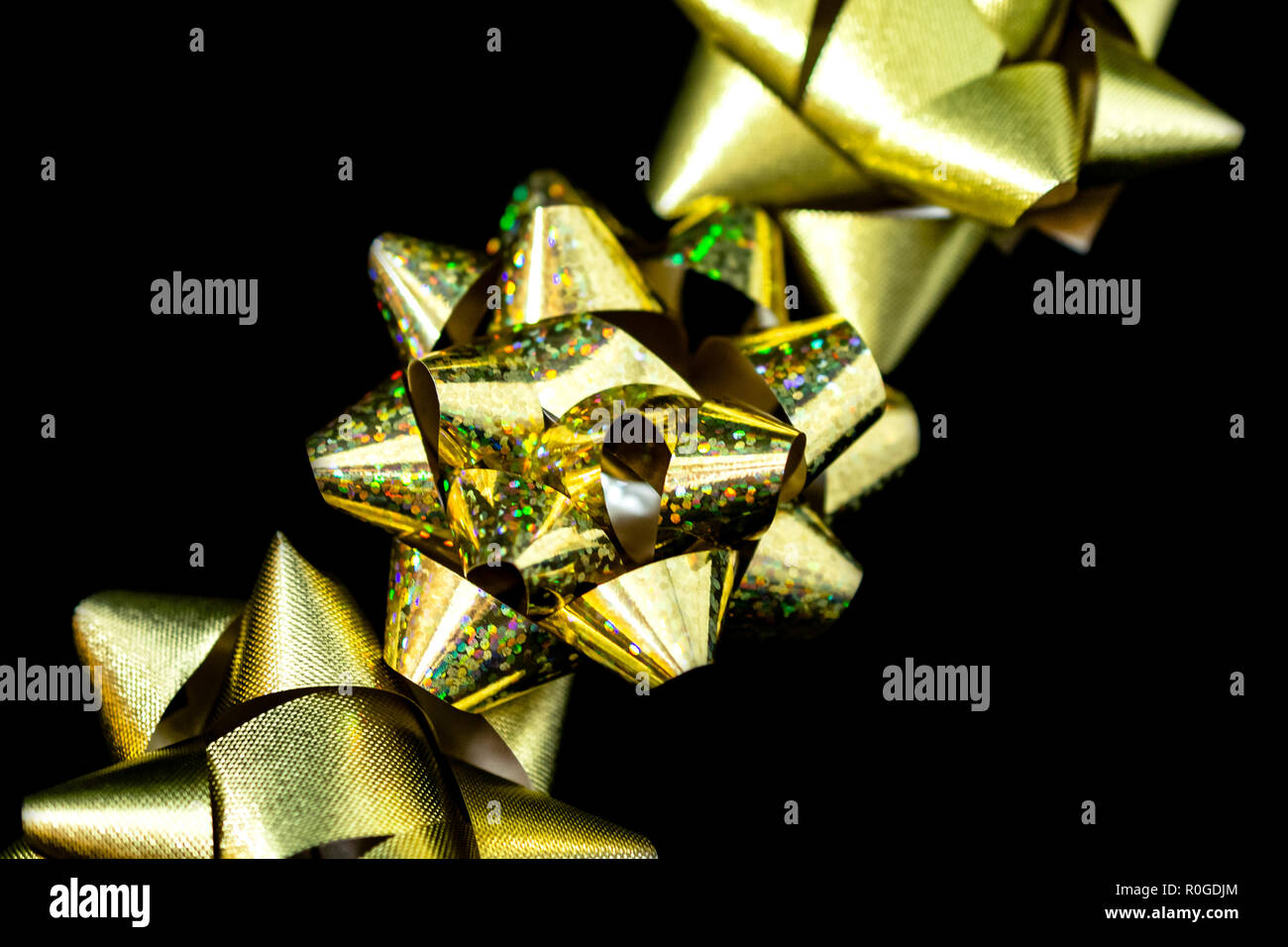 Tre (3) Vacanze di Natale in satin nastri Gold e Gold olografica a colori. Sfondo nero. Camera per copia. Foto Stock