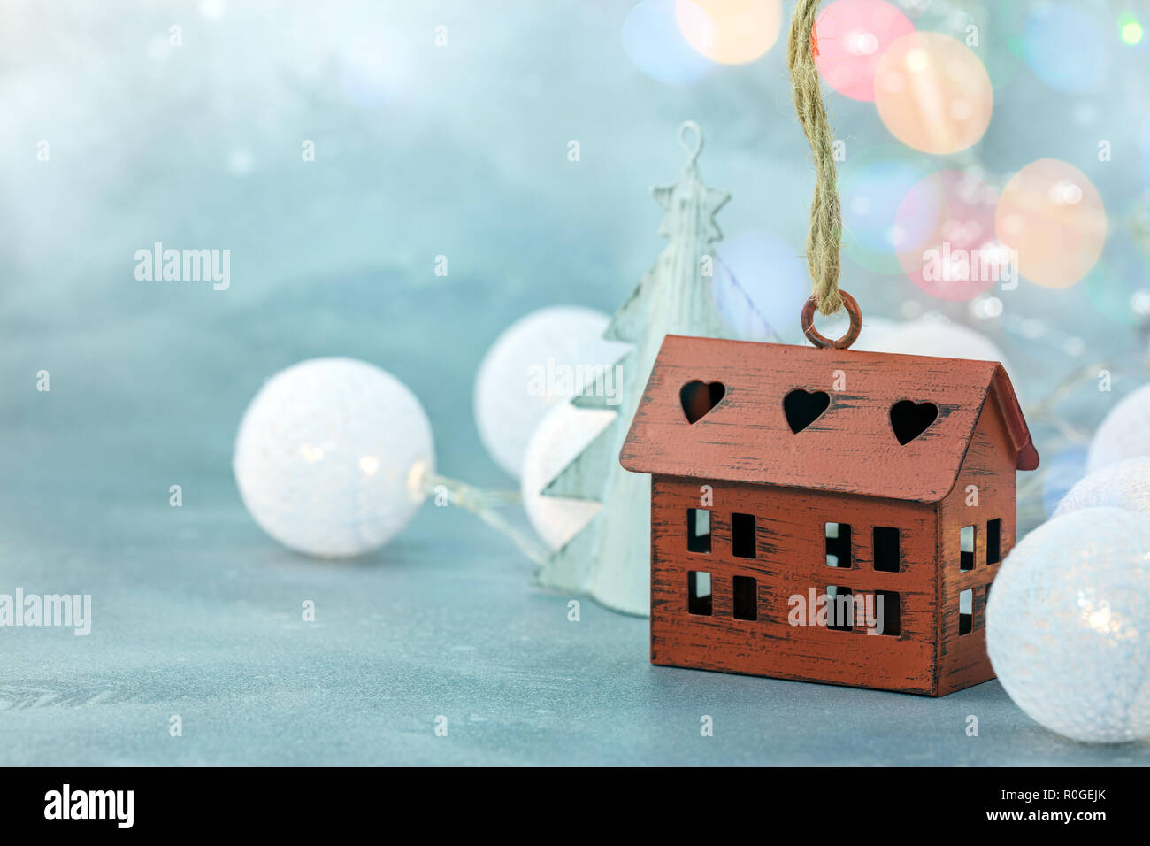Piccolo decorativi casa rossa con una ghirlanda palle luci su sfocato inverno sfondo blu Foto Stock