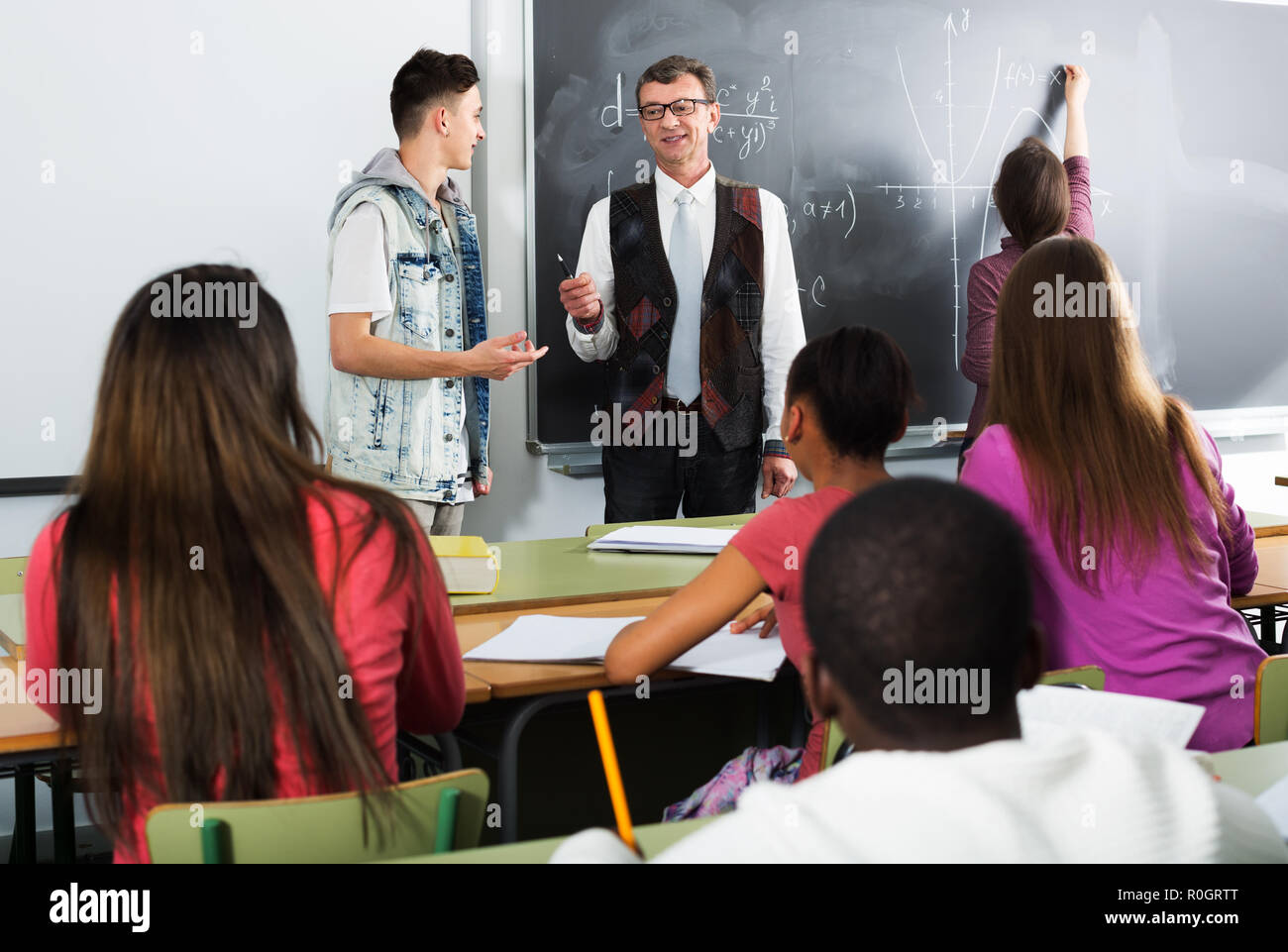 Gli studenti ascoltando la spiegazione e rispondendo ad un insegnante nella classe math Foto Stock