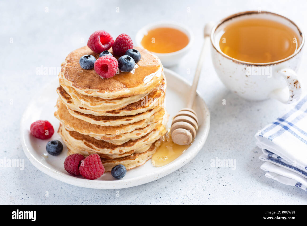 Pila di avena sana pancake con frutti di bosco, il miele e la tazza di tè verde su bianco sullo sfondo di calcestruzzo, il fuoco selettivo. Una gustosa colazione sana Foto Stock