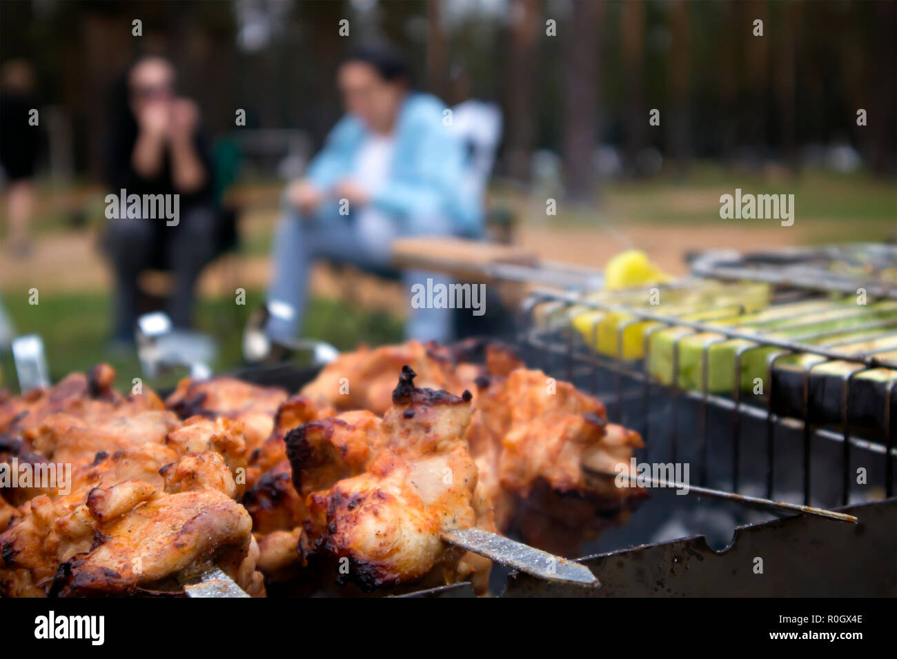 Spiedini con arrosti di carne di pollo sul grill caldo closeup con due sfocate sagome umane in background Foto Stock