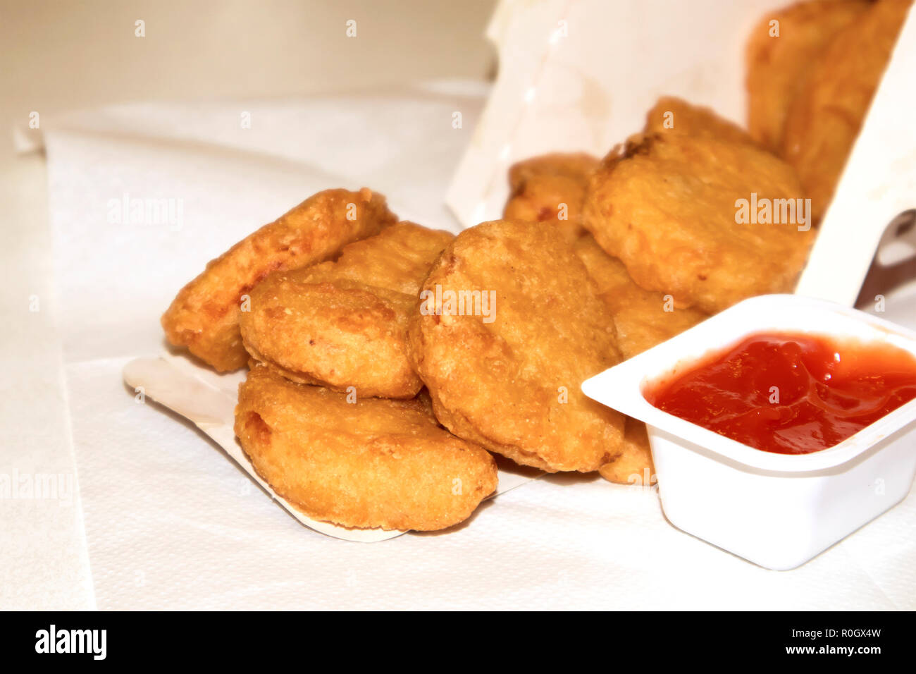 Pila di fritto di pollo croccante pepite fuoriuscita da una scatola di carta con ketchup Foto Stock