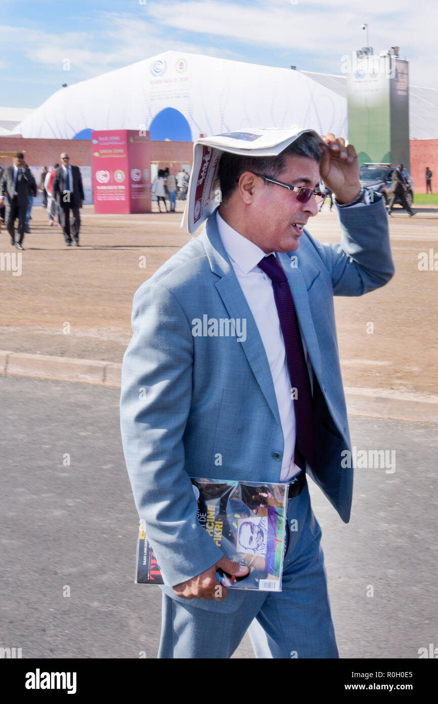 Nord Africano in pausa pranzo a piedi tenendo un Cambiamento Climatico brochure sopra la sua testa per evitare il sole di marrakech Africa del Nord Foto Stock