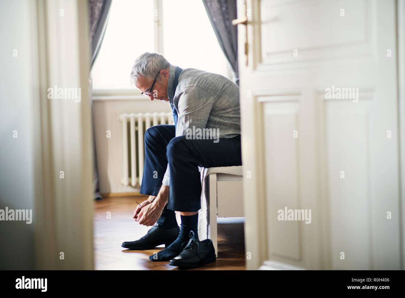 Imprenditore maturo su un viaggio di affari seduto in una stanza di un hotel, di legatura lacci delle scarpe. Foto Stock