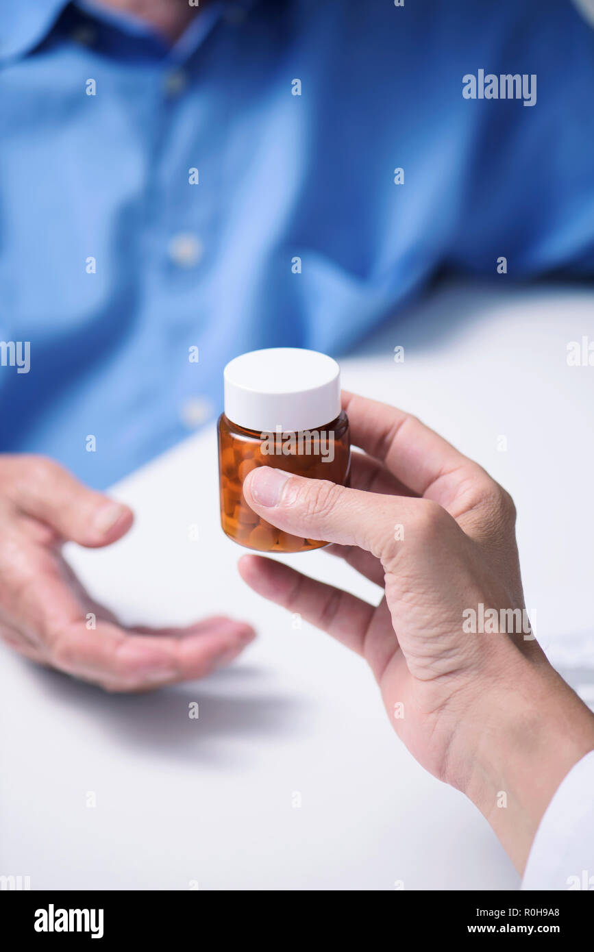 Primo piano di un medico caucasica uomo in camice bianco, dando una bottiglia di pillole a un senior caucasica uomo paziente, seduta sia in corrispondenza di un banco medici Foto Stock