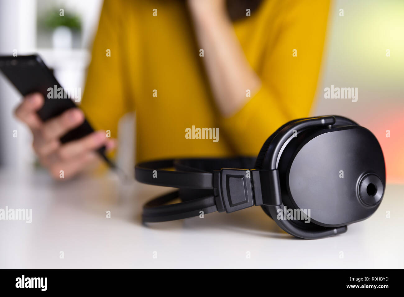 Cuffie su una tabella con sfondo colorato e una donna con un telefono intelligente nelle sue mani. Foto Stock
